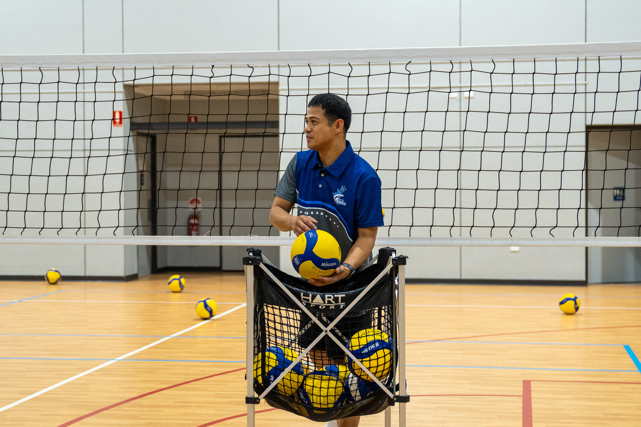 Sharks Volleyball coach holding a volleyball beside a ball trolley on court