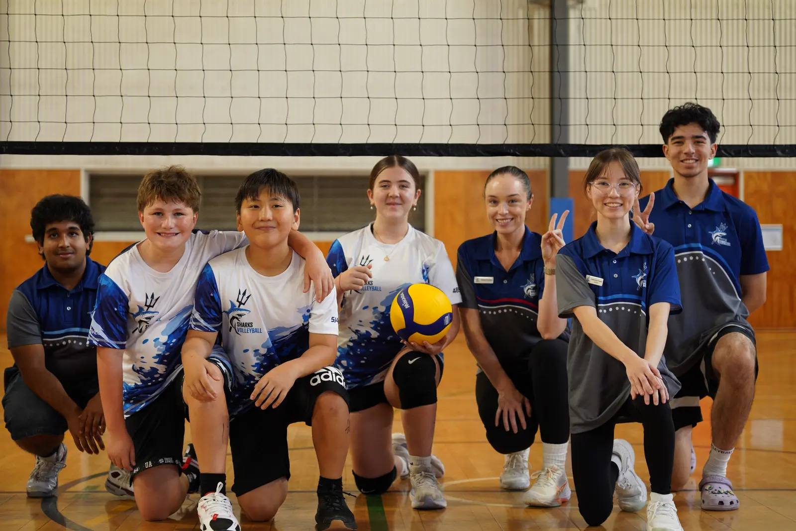 Sharks Volleyball athletes and coaches gathered together beside the net at camp